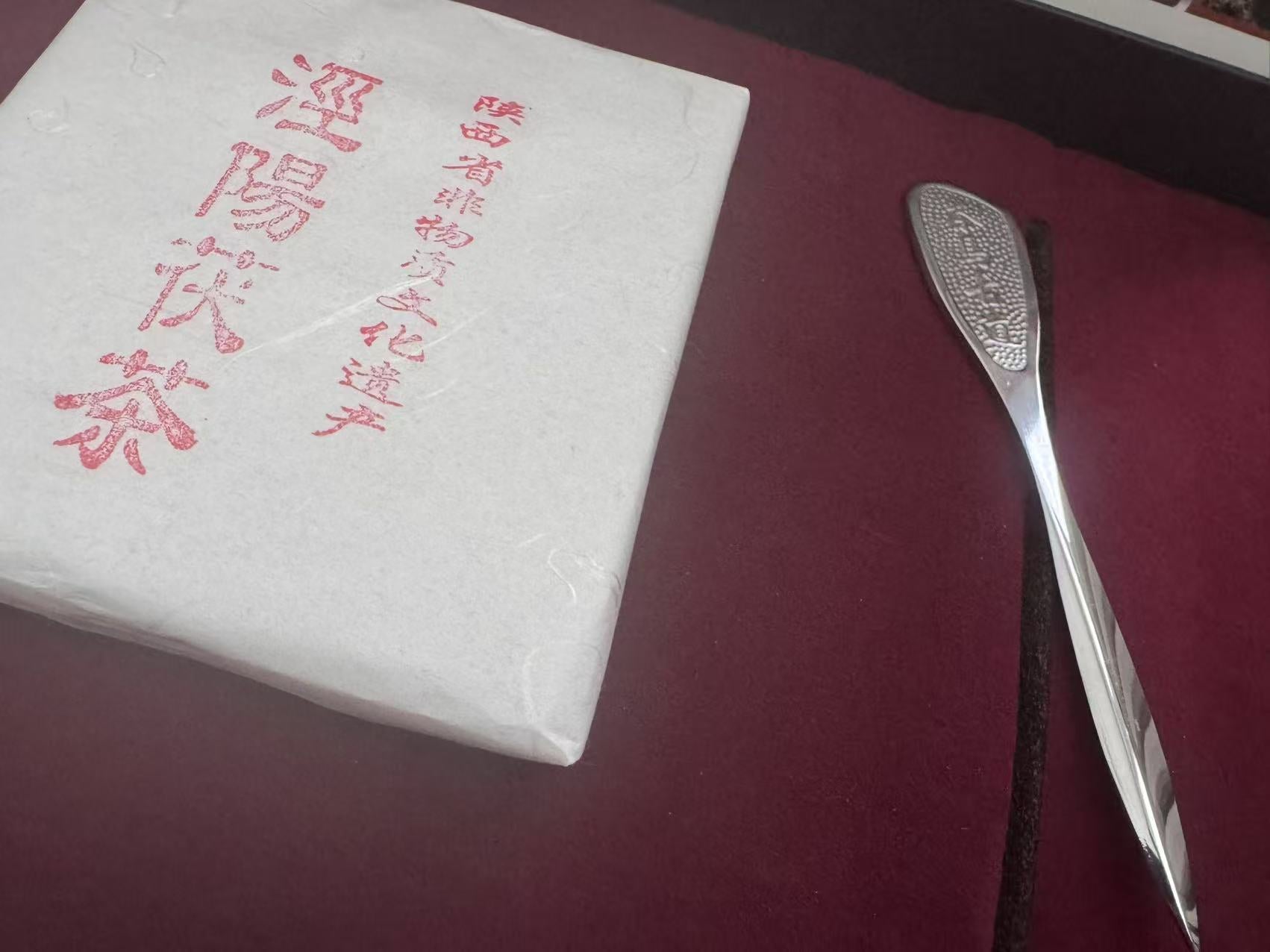 Verpackung des Jingwei Fu-Ziegeltees aus China neben einem Teelöffel auf einem samtigen Untergrund.