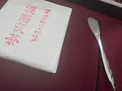 Verpackung des Jingwei Fu-Ziegeltees aus China neben einem Teelöffel auf einem samtigen Untergrund.